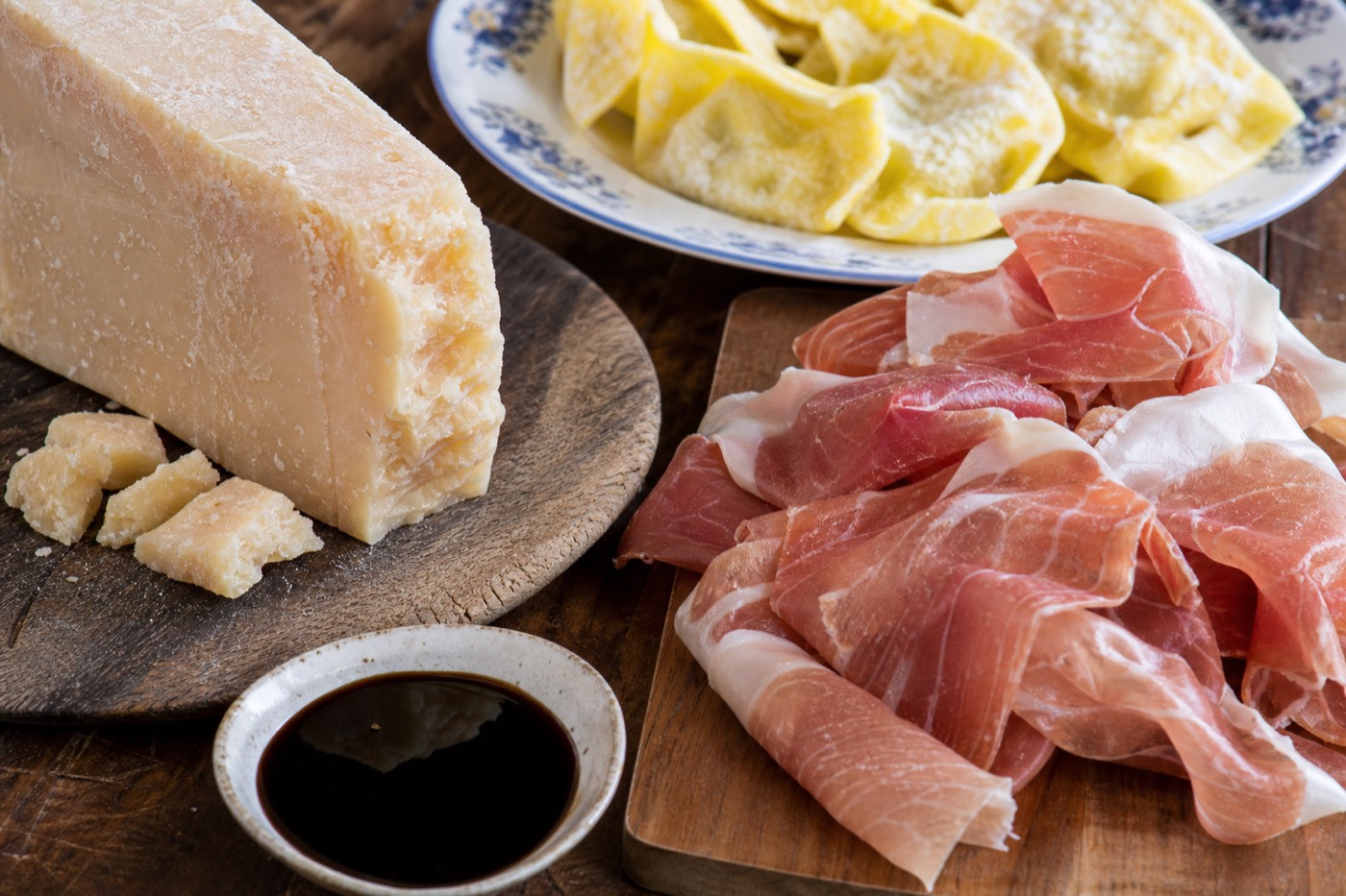 A wooden board with aged Parmigiano Reggiano wedges and thin Prosciutto di Parma slices, staples of what to eat in Parma